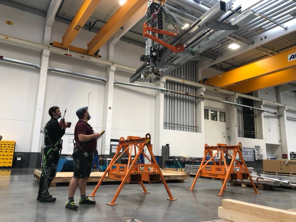 Tým techniků koordinující montáž konstrukce pod jeřábem.